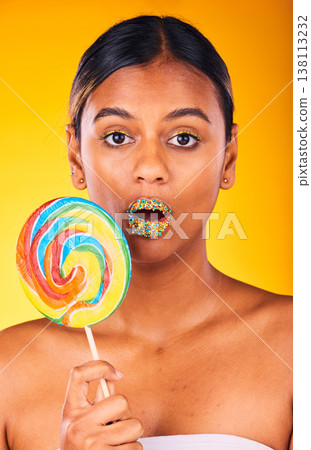 Shock, lollipop and portrait of woman in studio with makeup, cosmetic and face routine. Surprise, beauty and young Indian female model with colorful candy and facial cosmetology by yellow background. 138113232