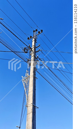 Utility pole features numerous power lines and cables against a bright blue sky, highlighting urban electrical infrastructure and connectivity Utility pole features numerous power lines and cables against a bright blue sky, highlighting urban electrical infrastructure and connectivity 138114210