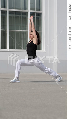 A woman stretches her body in an athletic pose in front of a contemporary building. This scene captures the dedication to maintaining fitness and the role of stretching in overall health. A woman stretches her body in an athletic pose in front of a contemporary building. This scene captures the dedication to maintaining fitness and the role of stretching in overall health. 138114388