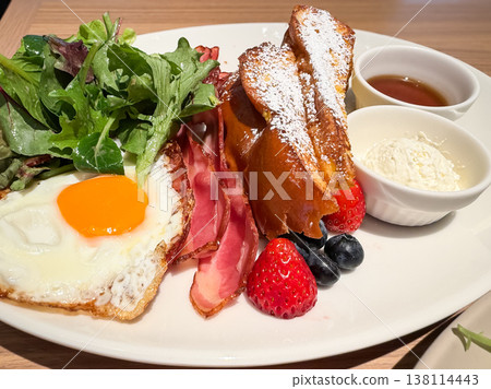 A plate dish topped with French toast, bacon, and a fried egg. A plate dish topped with French toast, bacon, and a fried egg. 138114443