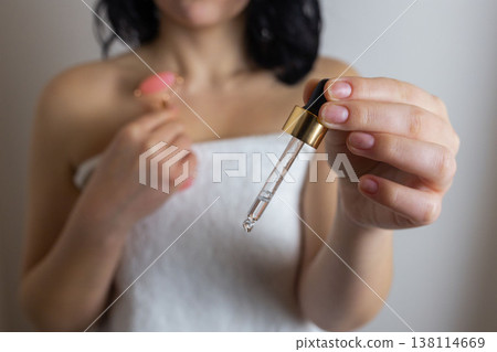 Woman holding facial roller and cosmetic serum dropper during skincare routine, beauty treatment and facial care concept 138114669