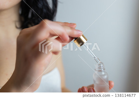 Woman using glass dropper to apply facial serum from cosmetic bottle, skincare routine and beauty treatment concept 138114677