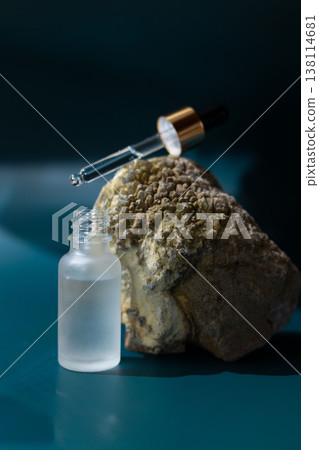 Frosted glass cosmetic dropper bottle on natural stone with dark blue background, skincare serum packaging mockup, minimal beauty product concept 138114681