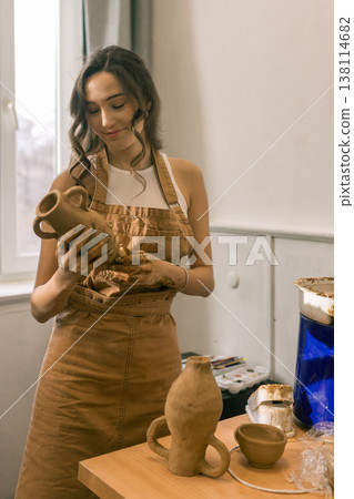 Young female ceramic artist holding handmade clay vase in pottery studio, creative craft process and handmade ceramics production 138114682
