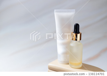 Cosmetic serum dropper bottle and skincare cream tube on minimal beige podium, beauty product packaging concept Cosmetic serum dropper bottle and skincare cream tube on minimal beige podium, beauty product packaging concept 138114701