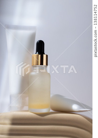 Cosmetic serum dropper bottle and skincare cream tube on minimal beige podium, beauty product packaging concept 138114752
