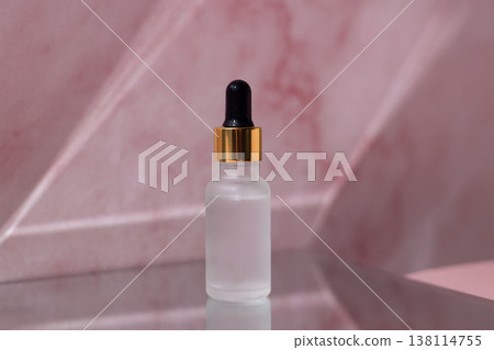 Cosmetic serum dropper with clear liquid and frosted glass bottle on pink reflective surface, skincare essence texture, beauty product concept Cosmetic serum dropper with clear liquid and frosted glass bottle on pink reflective surface, skincare essence texture, beauty product concept 138114755