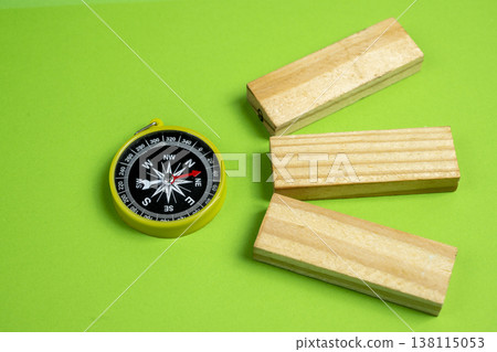 A yellow compass and three wooden blocks on a green background. Concept for navigation, strategy, and choosing the right path in business or education A yellow compass and three wooden blocks on a green background. Concept for navigation, strategy, and choosing the right path in business or education 138115053