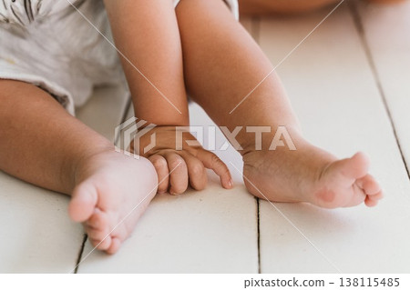 Close-Up of Baby Feet and Hand on White Wooden Floor Close-Up of Baby Feet and Hand on White Wooden Floor 138115485