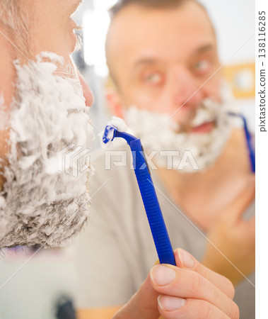 Guy shaving his beard in bathroom Guy shaving his beard in bathroom 138116285