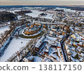 Aerial view of the historic town of s-Heerenberg in winter. Features the medieval Huis Bergh castle with its moat, a Gothic church, and snow covered rooftops under a bright seasonal sky. 138117150