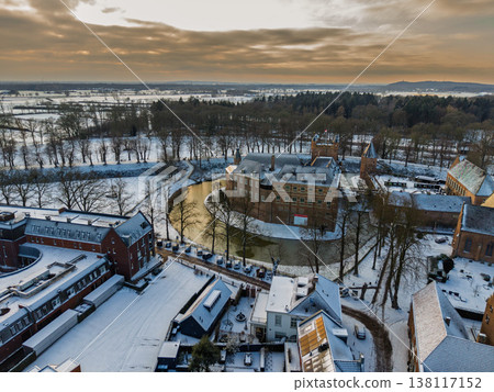 Detailed aerial view of Huis Bergh Castle in winter. Historical medieval brick fortress surrounded by a frozen circular moat and snow covered grounds in a picturesque European town landscape. 138117152