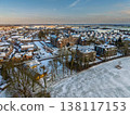 Aerial view of a historic brick building and modern residential district in a snowy Dutch landscape. Winter sunset over a European town with snow covered roofs, trees, and distant wind turbines. 138117153