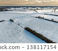 Aerial view of vast snow covered agricultural fields in the Dutch countryside at sunset. A minimalist winter landscape featuring frost, golden evening light, and a distant horizon under a hazy sky. 138117154