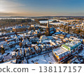 Aerial view of a picturesque snow covered European village at sunset, featuring a historic brick church with a tall spire, traditional red tiled roofs, and a peaceful winter landscape in Holland. 138117157