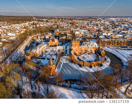 Aerial view of the medieval Huis Bergh Castle in s-Heerenberg, Netherlands. A stunning winter scene with a snow covered fortress, frozen moat, and a charming European town during golden hour. 138117159