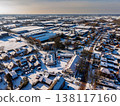 Aerial view of a snowy industrial and residential area in a Dutch town. Features snow covered factory warehouses, house construction sites, and suburban neighborhoods under a bright winter sun. 138117160