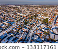 Aerial view of a dense residential neighborhood in a Dutch town after snowfall. A winter landscape featuring rows of red brick houses with snow covered roofs under a clear blue morning sky. 138117161