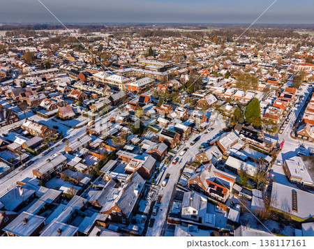 Aerial view of a dense residential neighborhood in a Dutch town after snowfall. A winter landscape featuring rows of red brick houses with snow covered roofs under a clear blue morning sky. Aerial view of a dense residential neighborhood in a Dutch town after snowfall. A winter landscape featuring rows of red brick houses with snow covered roofs under a clear blue morning sky. 138117161