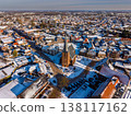 Aerial view of a snowy Dutch town square featuring a historic brick church with a tall spire. A beautiful winter landscape with snow covered roofs and traditional European architecture at sunrise. 138117162