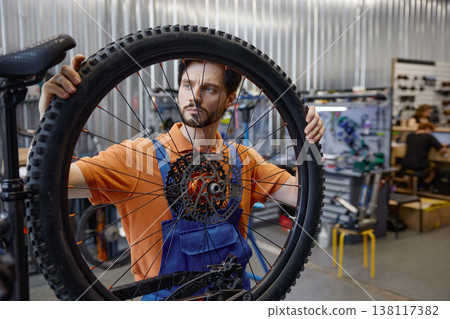 Technician analyzing bike wheel in repair shop environment Technician analyzing bike wheel in repair shop environment 138117382