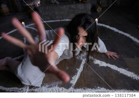 An anxious woman reaches out through chalk circle with candlelit surroundings An anxious woman reaches out through chalk circle with candlelit surroundings 138117384