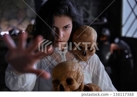 Enigmatic woman studies relic skulls in shadowed gothic room with mysterious ambiance Enigmatic woman studies relic skulls in shadowed gothic room with mysterious ambiance 138117388