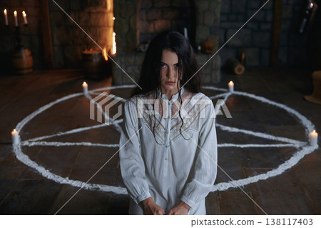 Woman practitioner in medieval chamber surrounded by candles and ancient artifacts 138117403