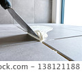 Tiling grey floor with white grout and steaming mortar 138121188