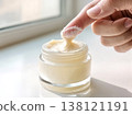 Finger Dipping into Glass Jar of Thick Moisturizing Face Cream 138121191