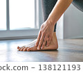 Close-up of a woman massaging her aching ankle and foot after a workout in a bright living room. 138121193