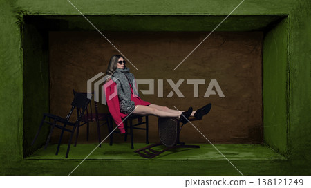 Woman in oversized scarf and sunglasses sitting on chairs inside box Woman in oversized scarf and sunglasses sitting on chairs inside box 138121249