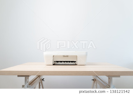 White all-in-one printer sits centered on a light wooden desk against a soft neutral wall, conveying minimalism, calm and productivity in a modern home office or small business workspace. 138121542