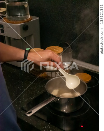 Man cooking soup in pot on induction stove in kitchen. Person using ladle to stir boiling liquid meal. Culinary process, homemade dinner preparation, domestic lifestyle concept. Man cooking soup in pot on induction stove in kitchen. Person using ladle to stir boiling liquid meal. Culinary process, homemade dinner preparation, domestic lifestyle concept. 138121551