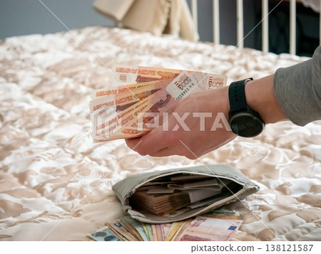 Man holding russian ruble banknotes over wallet on beige bedspread. Finance managing and spending cash. Wealth concept, savings, budget planning and home banking. Personal income concept. Man holding russian ruble banknotes over wallet on beige bedspread. Finance managing and spending cash. Wealth concept, savings, budget planning and home banking. Personal income concept. 138121587