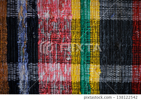 A horizontal top-down shot of a traditional handmade woven rug. The rug features vertical stripes in various colors, including red, yellow, green, black, and blue, with visible fabric textures. A horizontal top-down shot of a traditional handmade woven rug. The rug features vertical stripes in various colors, including red, yellow, green, black, and blue, with visible fabric textures. 138122542