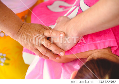 A horizontal top-down close-up shot of a therapist's hands performing a manual massage or osteopathic manipulation on a patient's shoulder. The patient is covered with a bright pink towel. 138122562