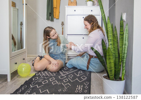 Two girls sitting with pet on a rug in a cozy room while one girl ties a bracelet Two girls sitting with pet on a rug in a cozy room while one girl ties a bracelet 138122587