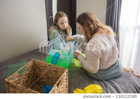 woman an girl sit on a bed in a room. Mom is holding a green hamster house with hamster woman an girl sit on a bed in a room. Mom is holding a green hamster house with hamster 138122590