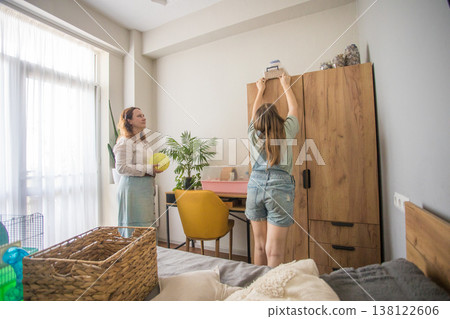 A woman and a girl are preparing a small cage in a well-lit room during the morning. A woman and a girl are preparing a small cage in a well-lit room during the morning. 138122606