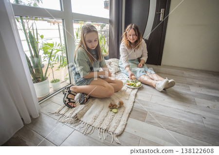 girl and women relax on a rug in a modern indoor space. They share snacks while sitting 138122608