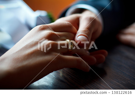 A horizontal close-up shot capturing a tender moment where one person holds another's hand, highlighting a gold wedding ring with an intricate pattern. A horizontal close-up shot capturing a tender moment where one person holds another's hand, highlighting a gold wedding ring with an intricate pattern. 138122616