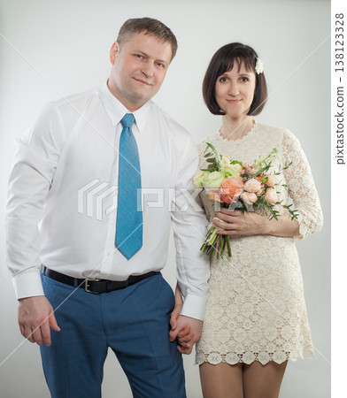 A woman holds a bouquet while hugging a man from behind in a studio. Both smile and look happy. A woman holds a bouquet while hugging a man from behind in a studio. Both smile and look happy. 138123328