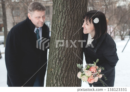 Couple enjoys a playful moment by a tree during winter in a snowy park  138123331