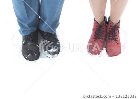 Two people stand together in snow with one wearing black shoes and the other in red boots. 138123332