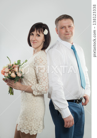 A woman holds a bouquet while hugging a man from behind in a studio. Both smile and look happy. A woman holds a bouquet while hugging a man from behind in a studio. Both smile and look happy. 138123338
