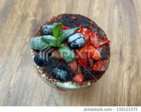 Dessert bowl with layers of cream, strawberries, blueberries, and mint on wooden table  138123375