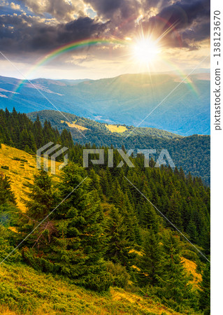 sunset over hillside of mountain range with coniferous forest and grassy meadow. beautiful summer landscape with alp. wonderful nature background of highland under rainbow for earth day sunset over hillside of mountain range with coniferous forest and grassy meadow. beautiful summer landscape with alp. wonderful nature background of highland under rainbow for earth day 138123670