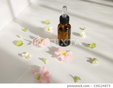 Organic essential oil bottle with glass dropper surrounded by spring flowers. Amber glass bottle with natural serum for skincare or aromatherapy on white surface with sunlight shadows. Organic essential oil bottle with glass dropper surrounded by spring flowers. Amber glass bottle with natural serum for skincare or aromatherapy on white surface with sunlight shadows. 138124873