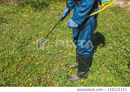 a man sprays herbicide over a grassy field a man sprays herbicide over a grassy field 138125352